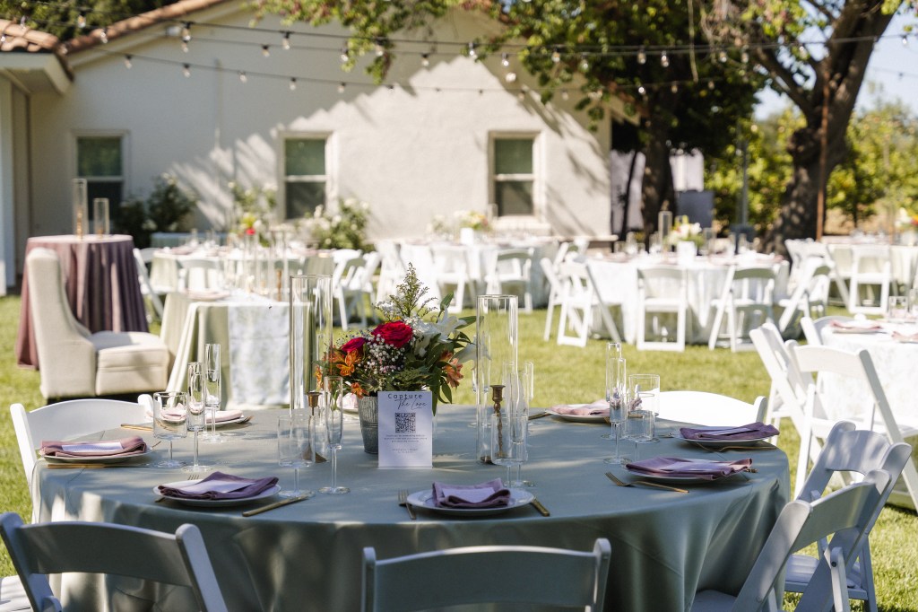 Outdoor event setup with decorated tables and floral centerpieces in a garden setting.