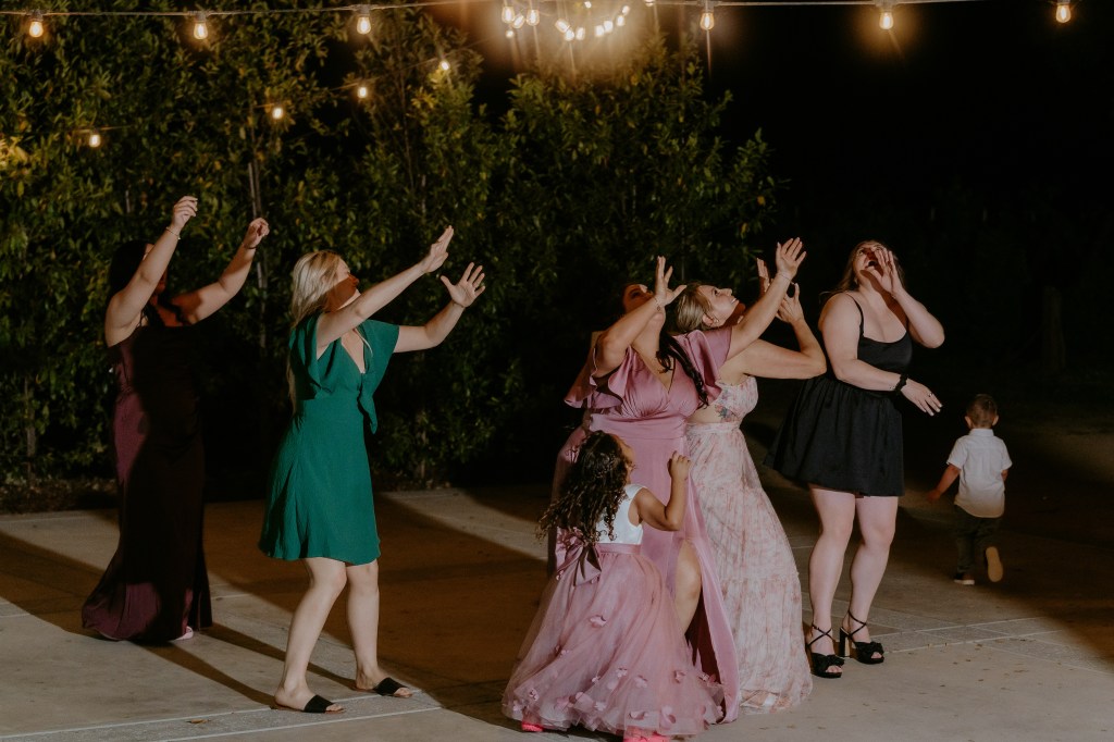 Group of women dancing joyfully under string lights at a nighttime outdoor event.