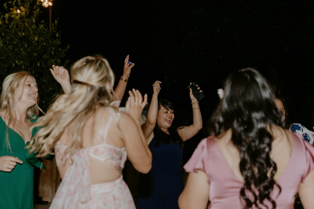 Group of women dancing joyfully at a nighttime celebration, with some raising their arms and smiling.